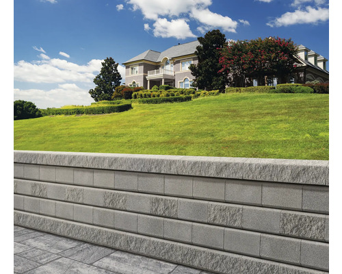 Mur de soutènement en blocs de pierre devant une maison sur une colline verdoyante