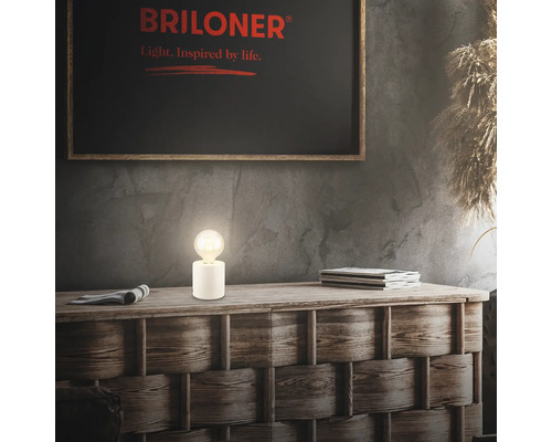 Dekorative Lampe auf Holzkommode mit Briloner Logo im Hintergrund