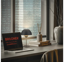 Tischszene mit Schreibtisch, Laptop mit Briloner Logo und stilvoller Tischleuchte vor einem Fenster