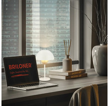 Tisch mit Laptop, Tischleuchte und Dekorationsartikeln vor Fenster