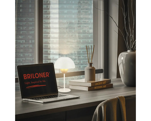 Tisch mit Laptop, Tischleuchte und Dekorationsartikeln vor Fenster