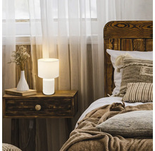 Schlafzimmerszene mit Nachttisch, Bett und einer weißen Tischleuchte