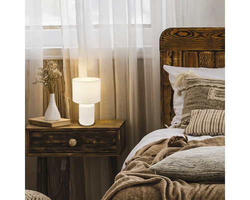 Schlafzimmerszene mit Nachttisch, Bett und einer weißen Tischleuchte