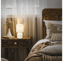 Schlafzimmer mit Nachttisch, Lampe, Bett und Vorhängen