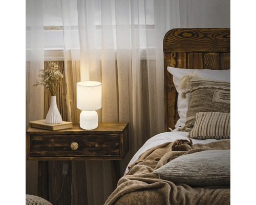 Schlafzimmer mit Nachttisch, Lampe, Bett und Vorhängen