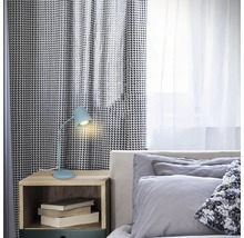 Schlafzimmerszene mit einem Nachttisch, auf dem eine blaue Schreibtischlampe und einige Bücher stehen.