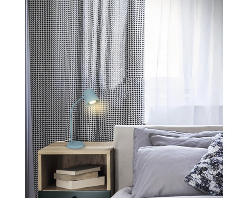 Schlafzimmerszene mit einem Nachttisch, auf dem eine blaue Schreibtischlampe und einige Bücher stehen.