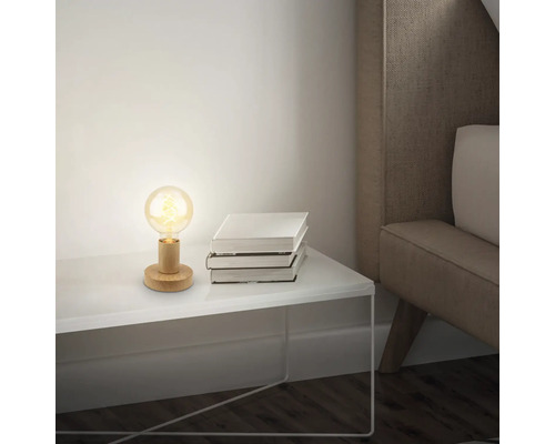 Tischleuchte mit Holzfuss und Glühbirne neben einem Stapel Bücher auf einem Nachttisch