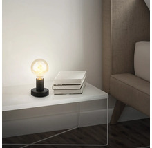 Tischleuchte mit Glühbirne auf Nachttisch neben einem Stapel Bücher