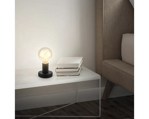 Tischleuchte mit Glühbirne auf Nachttisch neben einem Stapel Bücher