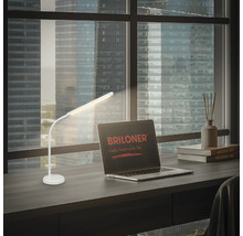 Weisse Schreibtischlampe auf einem Schreibtisch neben einem Laptop mit Briloner Logo.