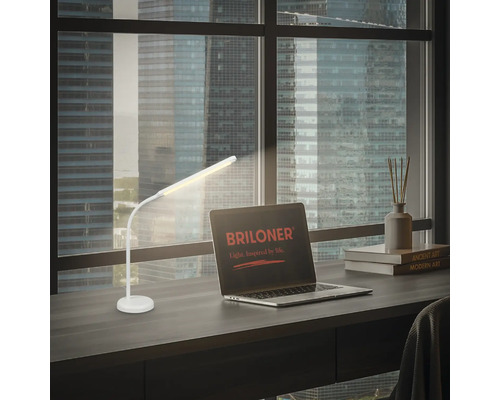 Weisse Schreibtischlampe auf einem Schreibtisch neben einem Laptop mit Briloner Logo.