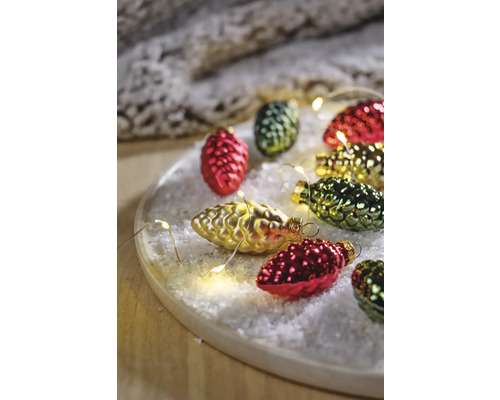 Weihnachtliche Szene mit Tannenzapfen-Christbaumschmuck und Lichterkette auf einem Teller mit Kunstschnee