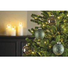 Nahaufnahme eines Weihnachtsbaums mit Christbaumkugeln und Lichtern, im Hintergrund sind Kerzen zu sehen