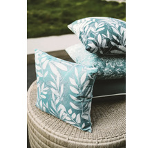 Dekokissen mit Blattmuster auf einem Korbtisch gestapelt