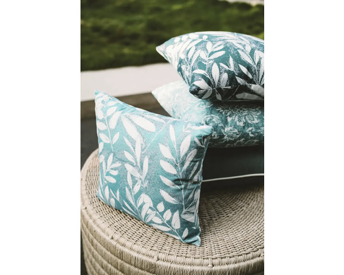 Dekokissen mit Blattmuster auf einem Korbtisch gestapelt