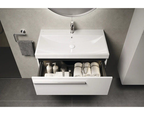 Meuble sous-lavabo avec tiroir ouvert, contenant des serviettes et des produits de soin dans la salle de bains.