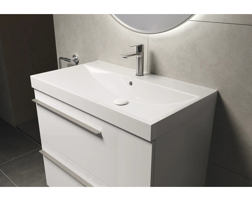 Meuble-lavabo blanc avec deux tiroirs, robinet et miroir rond avec rétroéclairage dans la salle de bains.