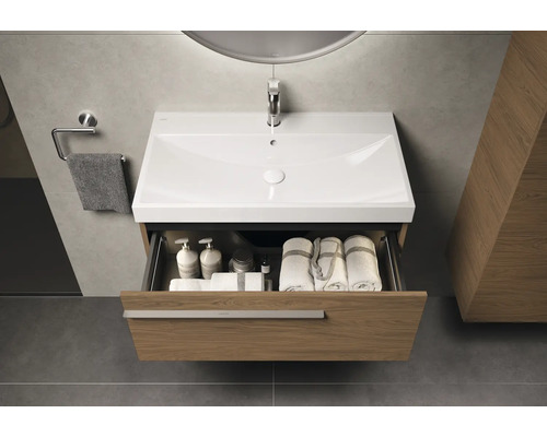 Meuble-lavabo avec tiroir ouvert, contenant des serviettes et des produits de soins, dans une salle de bain moderne