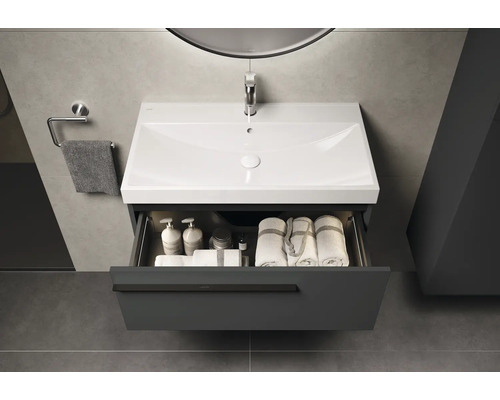 Meuble sous-lavabo avec tiroir ouvert, lavabo, serviettes et produits de soins dans la salle de bain