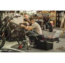 Deux hommes réparent une moto avec une boîte à outils dans un garage.