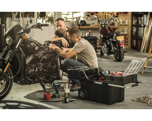 Deux hommes réparent une moto avec une boîte à outils dans un garage.