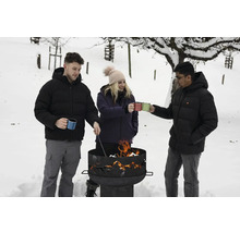 Drei Personen stehen im Schnee um eine Feuerschale und halten Tassen