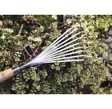 Balai à feuilles en métal avec manche en bois devant des plantes vertes