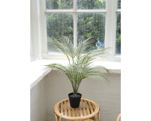 Palmier d'arec artificiel en pot sur une table en rotin devant une fenêtre