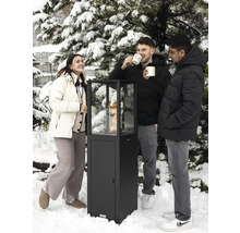 Trois personnes se tiennent dans la neige autour d'un chauffage de terrasse avec vitre.