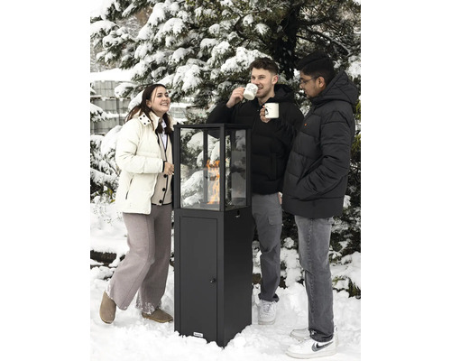 Trois personnes se tiennent dans la neige autour d'un chauffage de terrasse avec vitre.