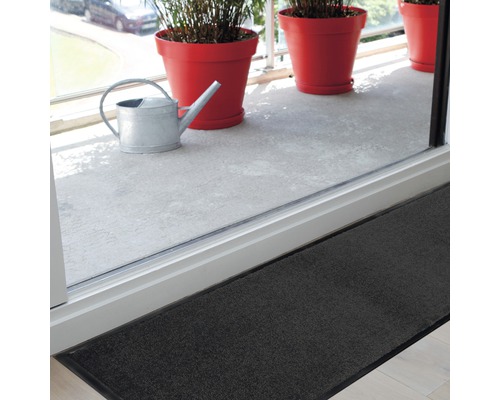 Dunkelgraue Fußmatte vor einer Balkontür mit Gießkanne und Blumentöpfen