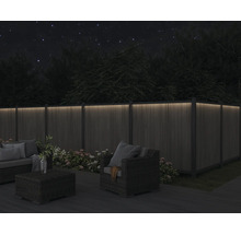 Eine Holzterrasse mit Loungemöbeln und einem beleuchteten Holzzaun bei Nacht.