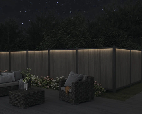 Eine Holzterrasse mit Loungemöbeln und einem beleuchteten Holzzaun bei Nacht.