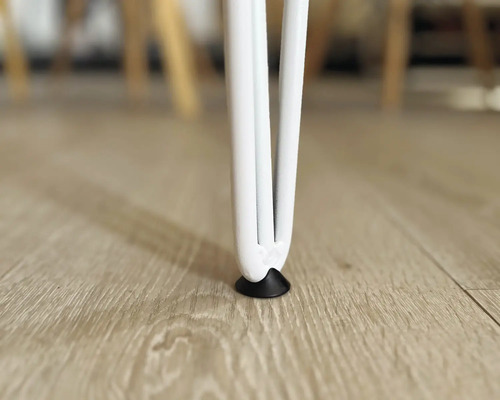 Detailaufnahme eines weissen Tischbeins mit Bodenschoner auf einem Holzboden.