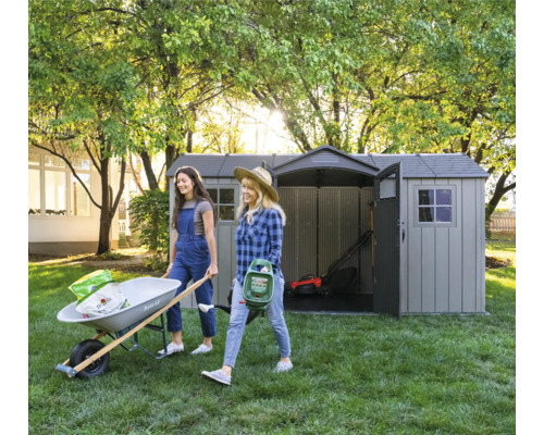 Scène de jardin avec deux femmes portant une brouette et un épandeur d'engrais, un abri de jardin en arrière-plan