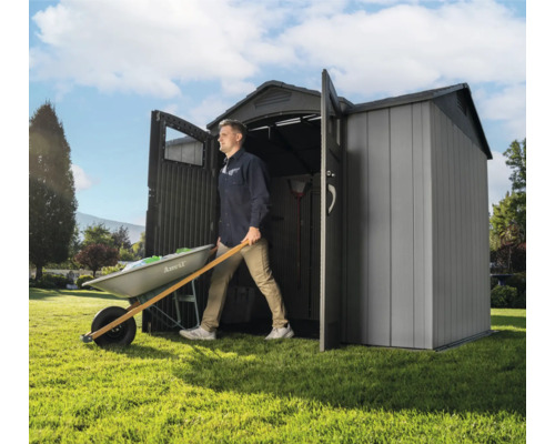 Un homme sort une brouette d'un abri de jardin