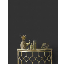 Ananas, flamant rose, singe, vase et figure géométrique décoratifs dorés sur une table d'appoint dorée devant un mur sombre.