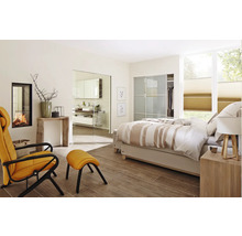 Chambre lumineuse avec cheminée, fauteuil et accès à la salle de bain par une porte en verre