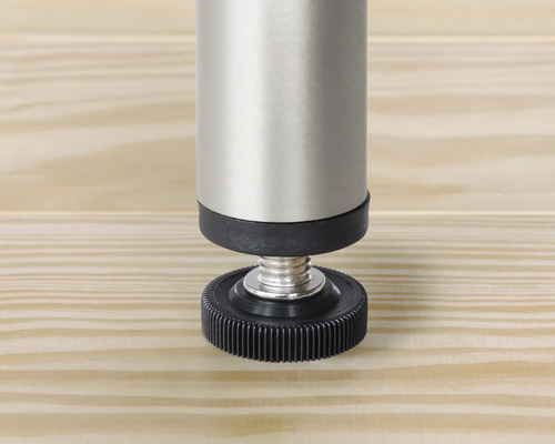 Vue détaillée d'un pied de meuble réglable en métal et plastique sur une surface en bois.