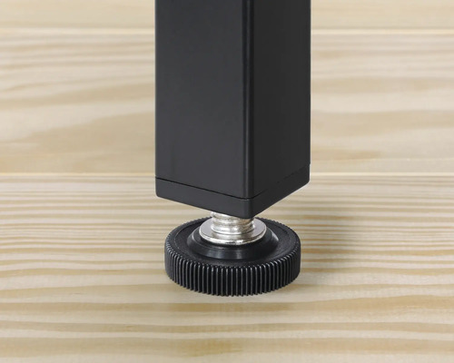 Vue détaillée d'un pied de table noir avec pied réglable sur un plancher en bois.