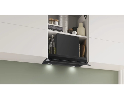 Eine Dunstabzugshaube ist unter einem Küchenschrank montiert und von Kochbüchern und anderen Küchenutensilien umgeben.