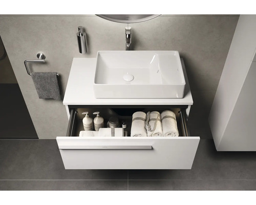 Meuble-lavabo avec tiroir ouvert contenant des serviettes et des produits de soins dans la salle de bain.