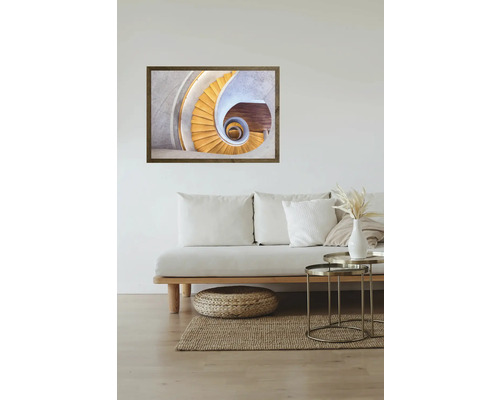 Une image encadrée d'un escalier en colimaçon est suspendue au-dessus d'un canapé dans un salon lumineux.