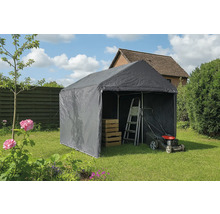 Tente de stockage grise dans le jardin avec échelle, tondeuse à gazon et caisses en bois