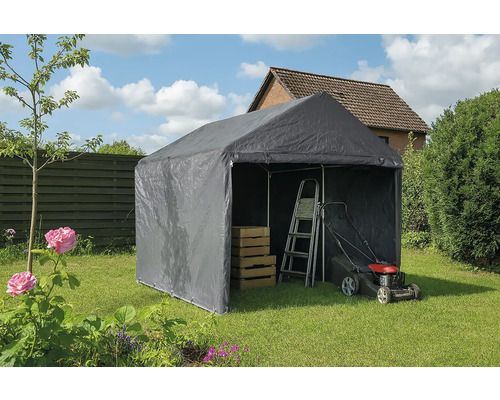 Tente de stockage grise dans le jardin avec échelle, tondeuse à gazon et caisses en bois