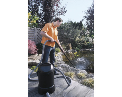 Un homme nettoie un bassin de jardin avec un aspirateur de bassin.