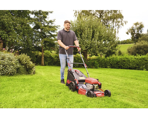 Ein Mann schiebt einen Rasenmäher auf einer Rasenfläche.