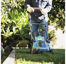 Eine Person mäht mit einem Makita Rasenmäher den Rasen im Garten.