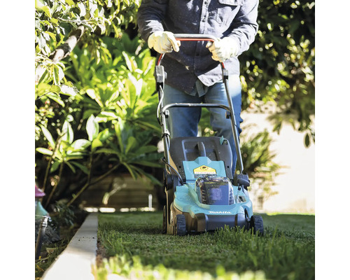 Eine Person mäht mit einem Makita Rasenmäher den Rasen im Garten.